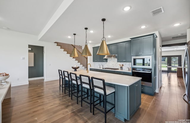 kitchen featuring a center island with sink, decorative light fixtures, decorative backsplash, wall oven, and a breakfast bar area