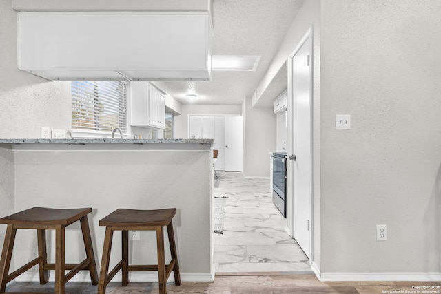 kitchen with white cabinets, a breakfast bar, light stone countertops, and kitchen peninsula