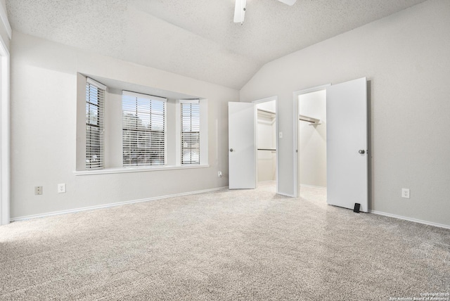 unfurnished bedroom with vaulted ceiling, ceiling fan, a spacious closet, a textured ceiling, and carpet floors