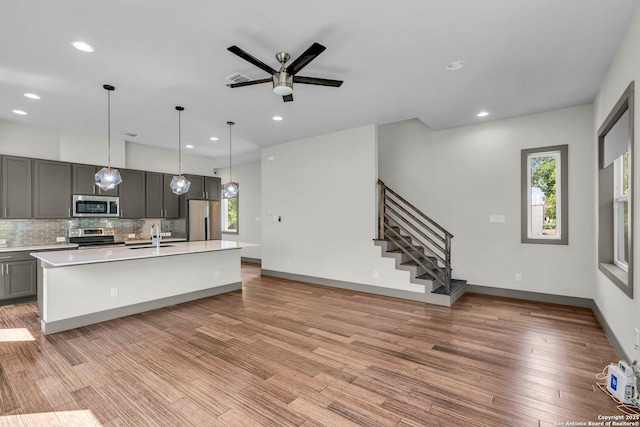 kitchen with decorative backsplash, stainless steel appliances, ceiling fan, gray cabinets, and an island with sink