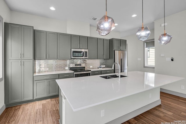 kitchen featuring gray cabinetry, sink, backsplash, a large island with sink, and appliances with stainless steel finishes