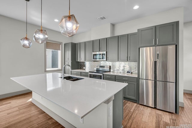 kitchen with a kitchen island with sink, sink, stainless steel appliances, and decorative light fixtures