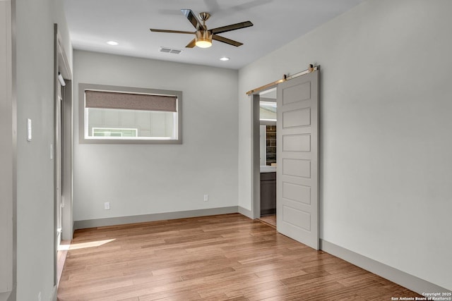 unfurnished bedroom with a barn door, ceiling fan, and light wood-type flooring