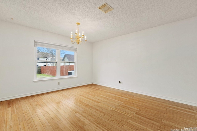 empty room with a textured ceiling, hardwood / wood-style flooring, and a notable chandelier