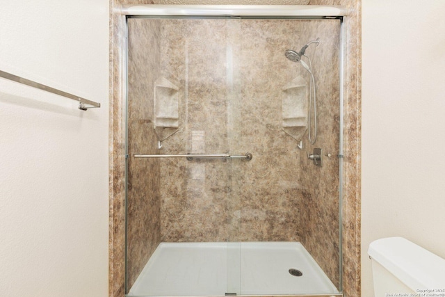 bathroom featuring a shower with door and toilet