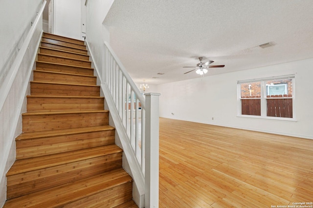 stairway featuring ceiling fan with notable chandelier, a textured ceiling, and hardwood / wood-style floors