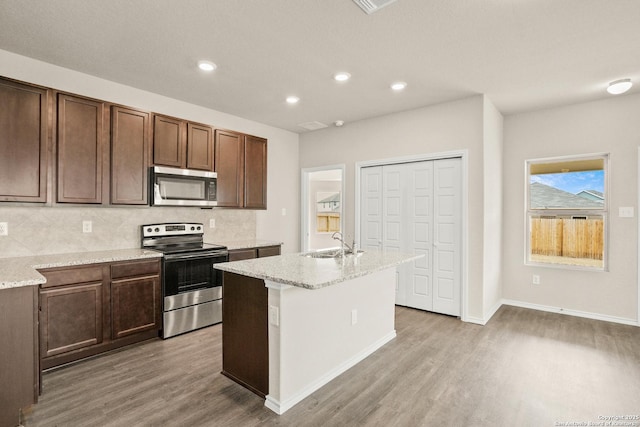 kitchen featuring appliances with stainless steel finishes, tasteful backsplash, a kitchen island with sink, sink, and light hardwood / wood-style flooring