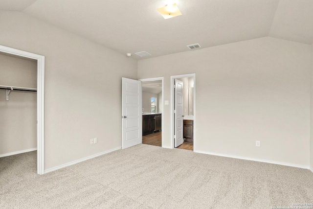 unfurnished bedroom featuring light carpet, ensuite bathroom, vaulted ceiling, a spacious closet, and a closet