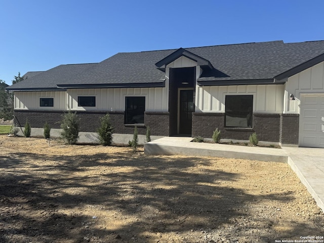 modern inspired farmhouse with board and batten siding, brick siding, a shingled roof, and a garage