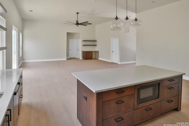 kitchen featuring pendant lighting, light countertops, a ceiling fan, a kitchen island, and black microwave