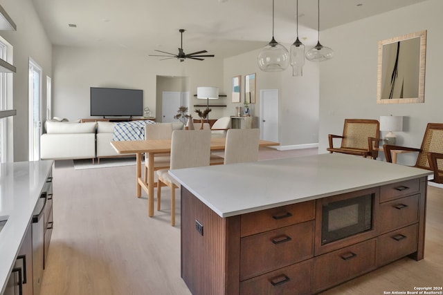 kitchen featuring ceiling fan, built in microwave, hanging light fixtures, a kitchen island, and light wood-type flooring