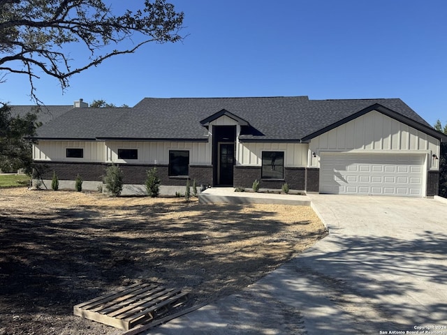 modern inspired farmhouse featuring concrete driveway, brick siding, roof with shingles, and an attached garage