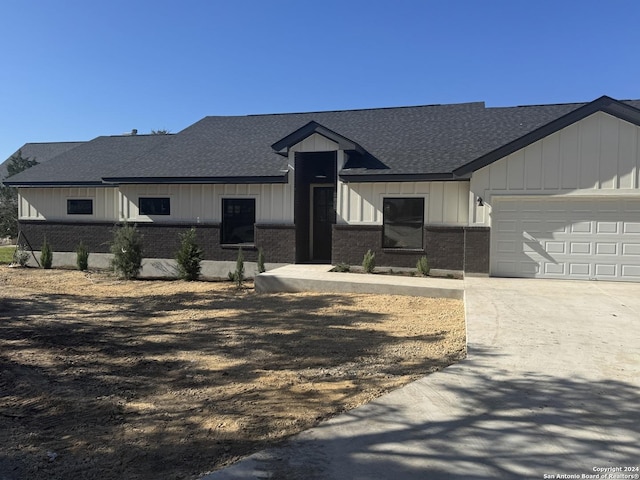 modern farmhouse featuring an attached garage, roof with shingles, concrete driveway, and brick siding