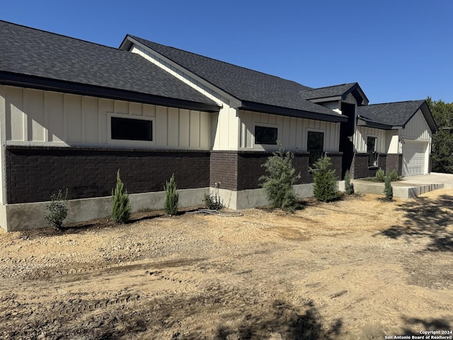 view of home's exterior with a garage, a shingled roof, board and batten siding, and brick siding