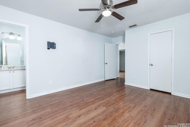 unfurnished bedroom featuring hardwood / wood-style flooring, ensuite bathroom, ceiling fan, and sink