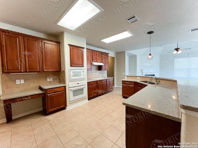 kitchen with kitchen peninsula, backsplash, light stone counters, white appliances, and decorative light fixtures