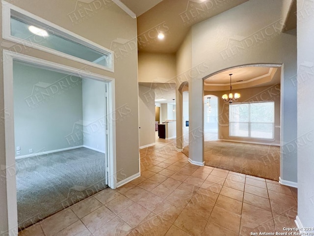 corridor featuring light tile patterned floors, an inviting chandelier, a raised ceiling, and crown molding