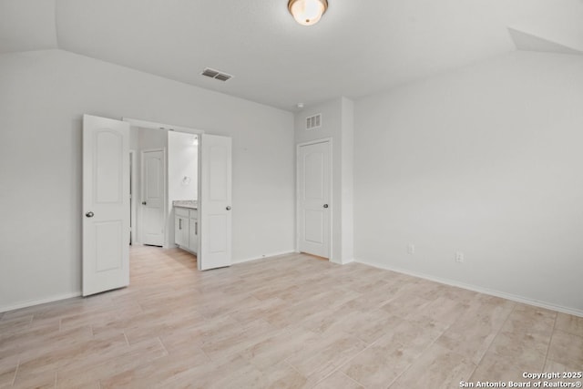 unfurnished bedroom featuring ensuite bathroom and lofted ceiling