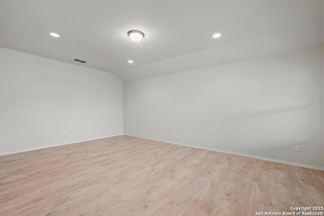 spare room with light wood-type flooring and lofted ceiling