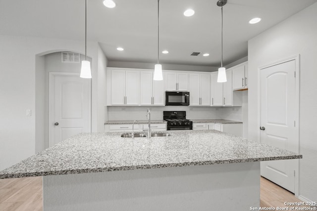 kitchen featuring white cabinetry, sink, an island with sink, pendant lighting, and black appliances