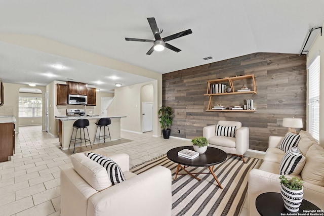 living room with ceiling fan, wood walls, light tile patterned flooring, and vaulted ceiling