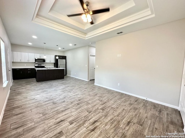 kitchen with appliances with stainless steel finishes, a raised ceiling, hardwood / wood-style flooring, white cabinets, and a kitchen island