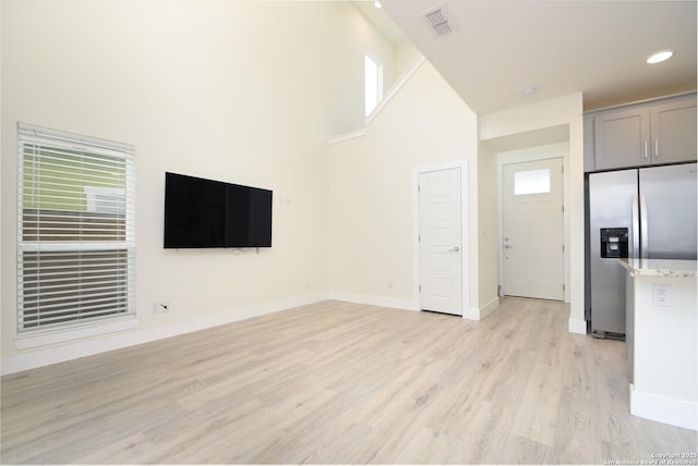 unfurnished living room featuring light wood-type flooring and a towering ceiling