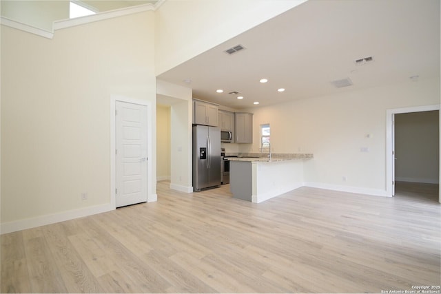 kitchen with kitchen peninsula, light wood-type flooring, light stone counters, stainless steel appliances, and gray cabinets