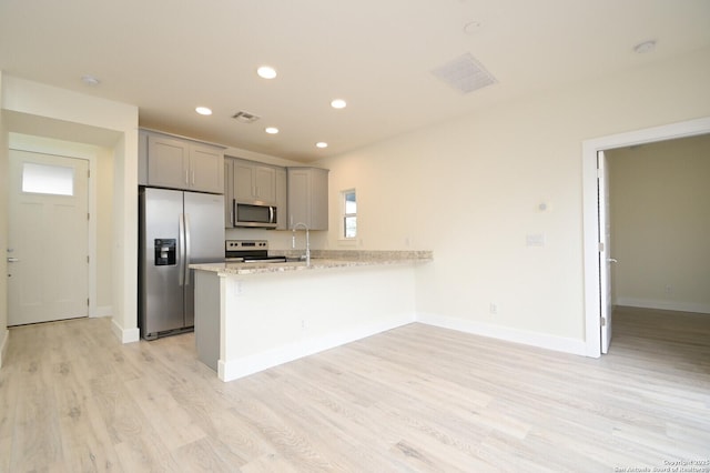 kitchen with light stone countertops, kitchen peninsula, light wood-type flooring, gray cabinetry, and stainless steel appliances