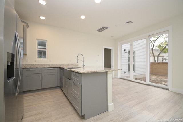 kitchen with sink, stainless steel fridge, light wood-type flooring, light stone counters, and kitchen peninsula