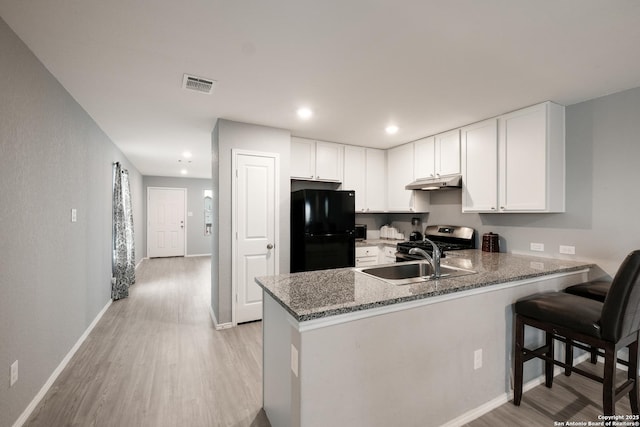 kitchen featuring white cabinets, black refrigerator, stainless steel gas stove, sink, and kitchen peninsula