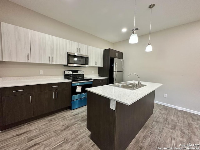 kitchen with a kitchen island with sink, sink, appliances with stainless steel finishes, decorative light fixtures, and wood-type flooring