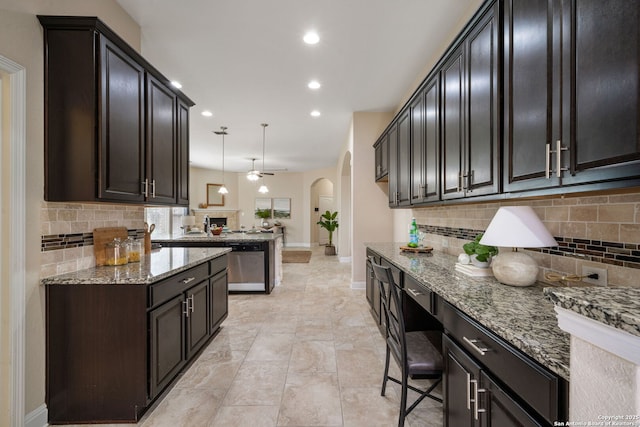 kitchen with light stone countertops, backsplash, stainless steel dishwasher, ceiling fan, and decorative light fixtures