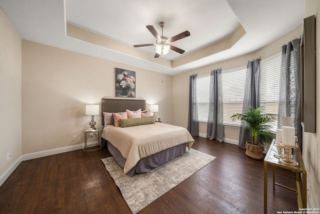 bedroom with ceiling fan, dark hardwood / wood-style floors, and a tray ceiling