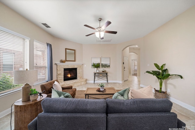 tiled living room featuring a stone fireplace and ceiling fan