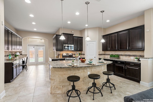 kitchen with light stone countertops, appliances with stainless steel finishes, a center island, and decorative light fixtures