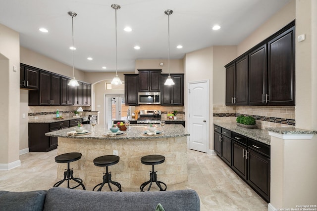 kitchen featuring pendant lighting, light stone countertops, dark brown cabinets, a kitchen island, and stainless steel appliances