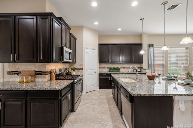 kitchen featuring pendant lighting, backsplash, light stone counters, dark brown cabinetry, and stainless steel appliances