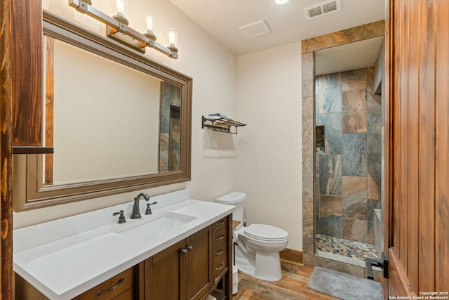 bathroom with a tile shower, hardwood / wood-style flooring, vanity, and toilet