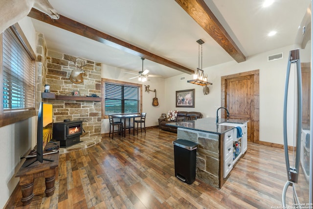 kitchen featuring beamed ceiling, a wood stove, ceiling fan, and dark wood-type flooring