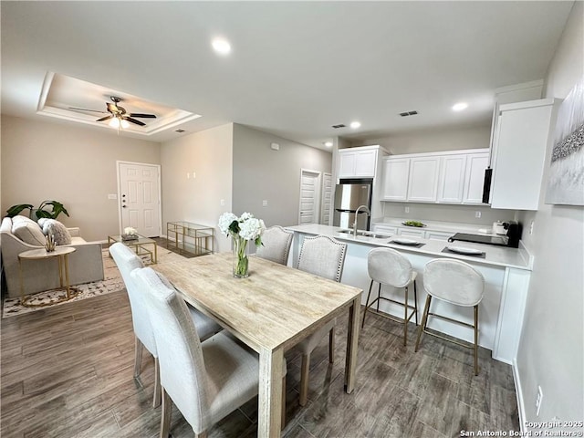 dining area with ceiling fan, a raised ceiling, and sink