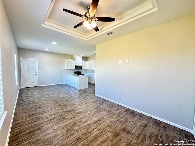 unfurnished living room with hardwood / wood-style floors, a tray ceiling, and ceiling fan