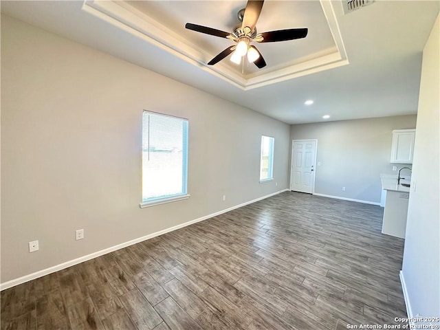 empty room featuring dark hardwood / wood-style flooring, a tray ceiling, ceiling fan, and sink