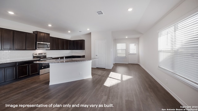 kitchen featuring appliances with stainless steel finishes, backsplash, light stone counters, a kitchen island with sink, and dark hardwood / wood-style floors