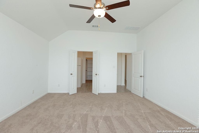 unfurnished bedroom featuring a walk in closet, ceiling fan, light carpet, and vaulted ceiling