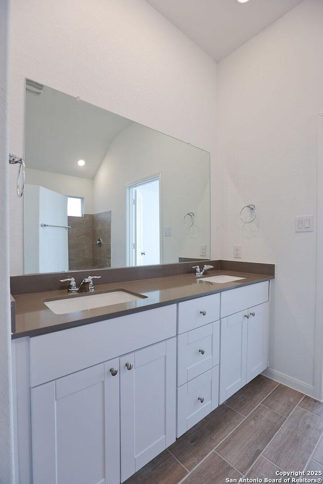 bathroom with a tile shower, vanity, and vaulted ceiling