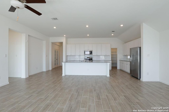 kitchen with stainless steel appliances, white cabinetry, tasteful backsplash, and an island with sink