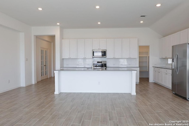 kitchen featuring backsplash, stainless steel appliances, a center island with sink, light hardwood / wood-style flooring, and white cabinetry