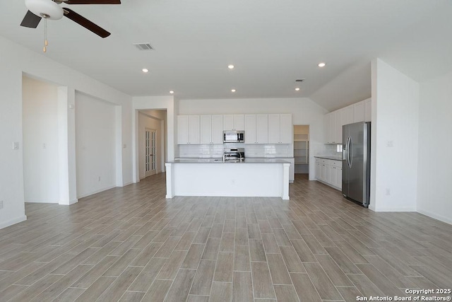 kitchen with a kitchen island with sink, white cabinets, decorative backsplash, ceiling fan, and appliances with stainless steel finishes