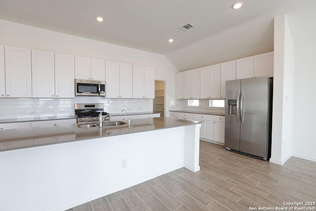 kitchen featuring appliances with stainless steel finishes, backsplash, sink, white cabinetry, and lofted ceiling